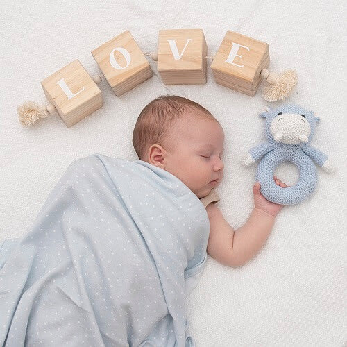 baby in swaddle holding hippo knitted rattle