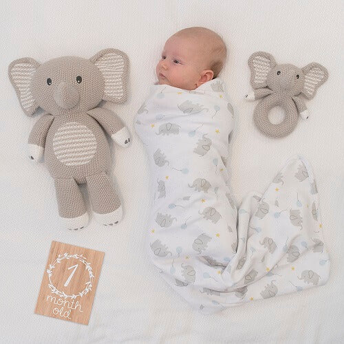 baby in swaddle with knitted elephant toy and rattle