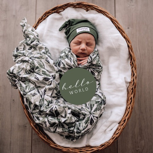 baby in evergreen swaddle with olive milestone card